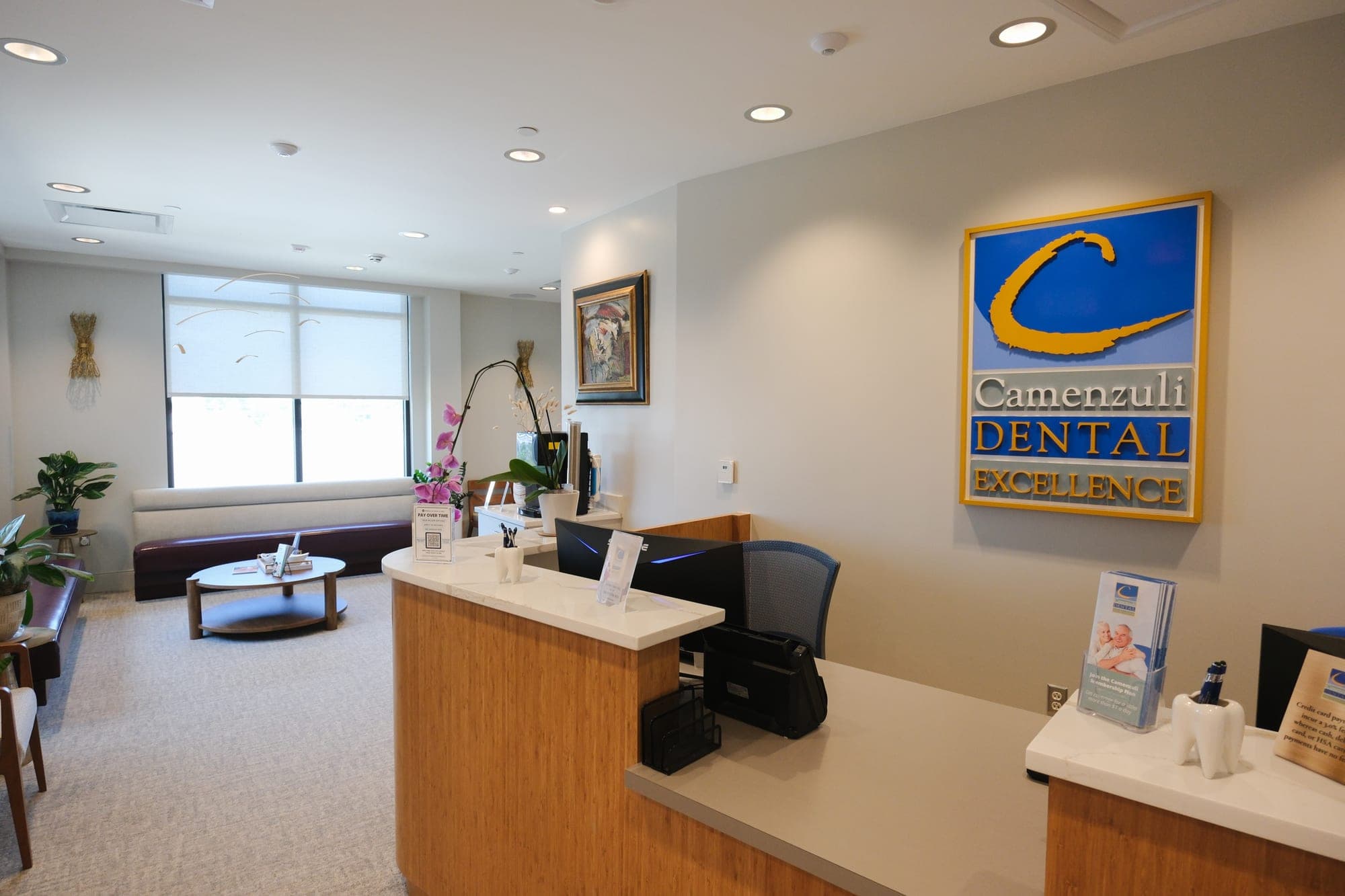 The front desk and waiting lounge at Camenzuli Dental Excellence, beneath the practice's logo sign