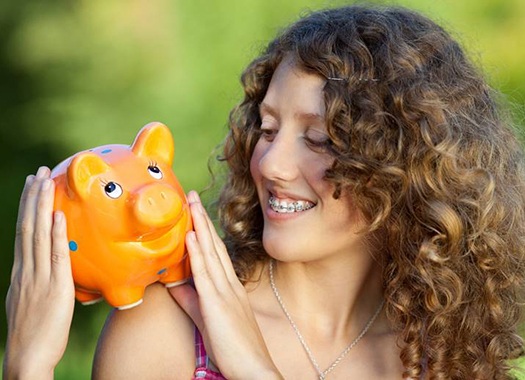Smiling girl with braces holding piggy bank symbolizing cost