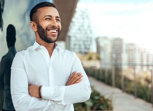 a person smiling and standing outside with their arms crossed