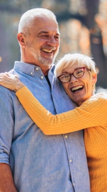 Older man and woman outdoors smiling and hugging