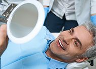 A middle-aged man looking at his new smile in the mirror while at the dentist’s office