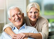 An older couple hugs and smiles after receiving their dental implants