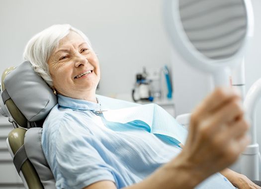 older woman admiring her smile with implant-retained dentures in New Orleans