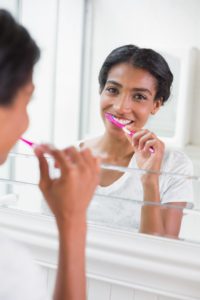 woman brushing teeth in mirror